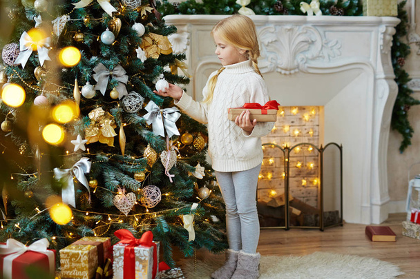 Mignon enfant en tenue de maison debout par sapin décoré et cheminée sur la nuit de Noël
 - Photo, image