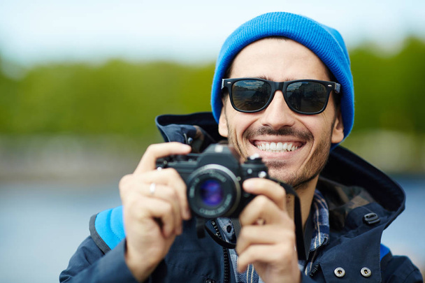 Retrato de un joven feliz tomando fotos con cámara fotográfica disfrutando de un viaje de senderismo en la naturaleza
 - Foto, imagen