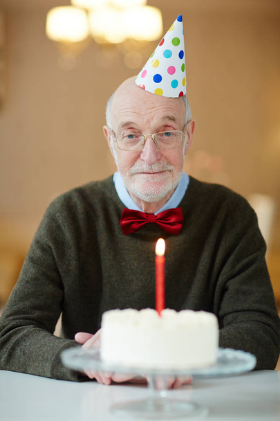 Sad senior man sitting by table with birthday cake - Фото, изображение