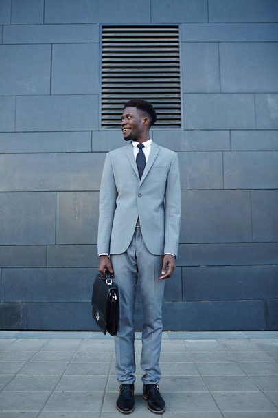 glücklicher afrikanischer Mann in Formalbekleidung steht gegen Hauswand - Foto, Bild