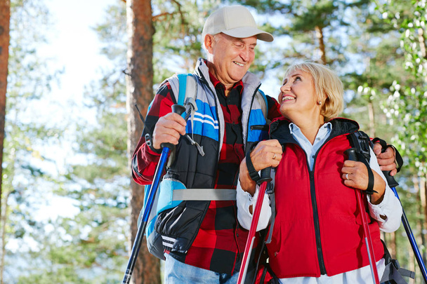 Personas mayores cariñosas con bastones de trekking mirándose
 - Foto, imagen