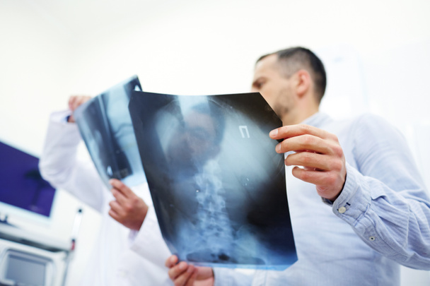 Χαμηλή οπτική γωνία αγνώριστος ιατρού και του ασθενή που συζητάμε X-ray εικόνες κατά τη διάρκεια συνάντησης στο σύγχρονο γραφείο, επικεντρωθεί σε πρώτο πλάνο - Φωτογραφία, εικόνα