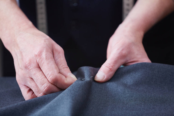 Closeup de alfaiate qualificado irreconhecível trabalhando no atelier: mãos costurando tecido enquanto costura roupas na mesa
 - Foto, Imagem