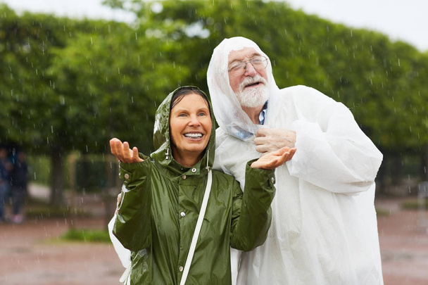 Happy senior couple enjoying rainfall on summer day - Фото, зображення