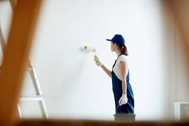 Portrét mladé ženy na staveništi: zaměstnankyně Malování zdi bílé, pomocí programu Malování válečkem při remodelaci úřadu - Fotografie, Obrázek