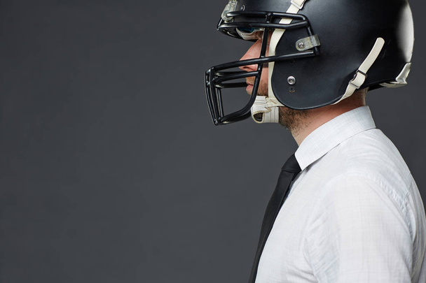 Side view portrait of middle-aged businessman wearing American football helmet against grey background, copy space to left - Photo, Image