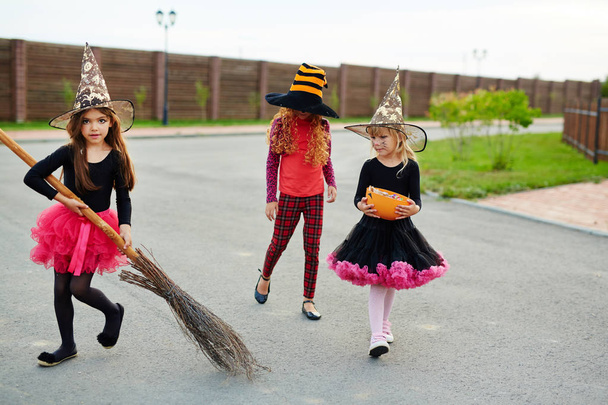 Pequeña bruja con escoba y sus amigos caminando por el camino en la noche de Halloween
 - Foto, Imagen