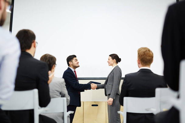 Vista del perfil de los alegres socios de negocios estrechando la mano mientras están de pie en la pizarra interactiva en la sala de conferencias
 - Foto, imagen