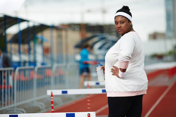 Tlustá žena s lahví vody stojí mezi překážky na stadionu - Fotografie, Obrázek