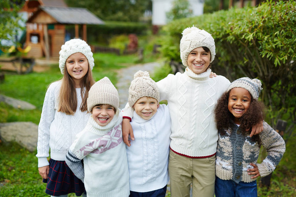 Ευτυχισμένα παιδιά διαφόρων ηλικιών στέκονται κοντά μαζί και βλέπουν φωτογραφική μηχανή χαμογελώντας, ντυμένοι στα λευκά ενδύματα δεμένη θέτοντας ως αδέλφια ή οικογένεια ταιριάσματος - Φωτογραφία, εικόνα