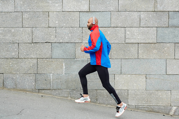 Actieve jongeman in sportkleding joggen langs de muur - Foto, afbeelding