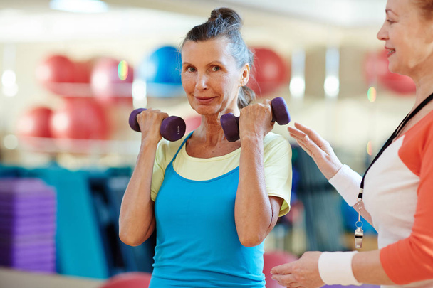 Aged woman looking at camera while exercising in gym - Photo, Image
