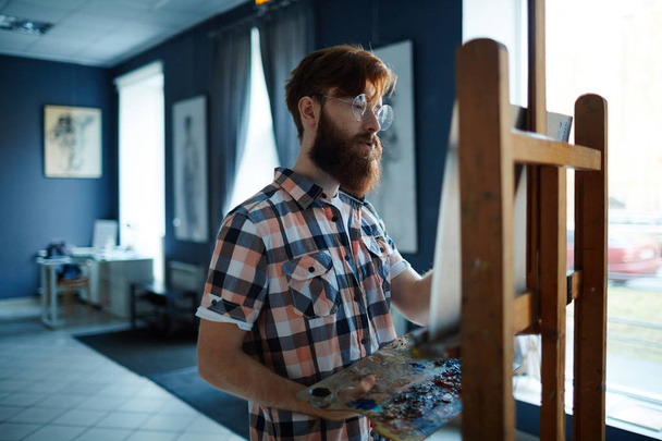 Jeune homme apprenant à peindre sur chevalet avec des peintures acrylliques
 - Photo, image