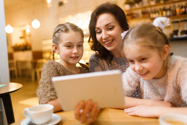 Jovem feliz com touchpad mostrando seu filme filhas gêmeas para crianças
 - Foto, Imagem