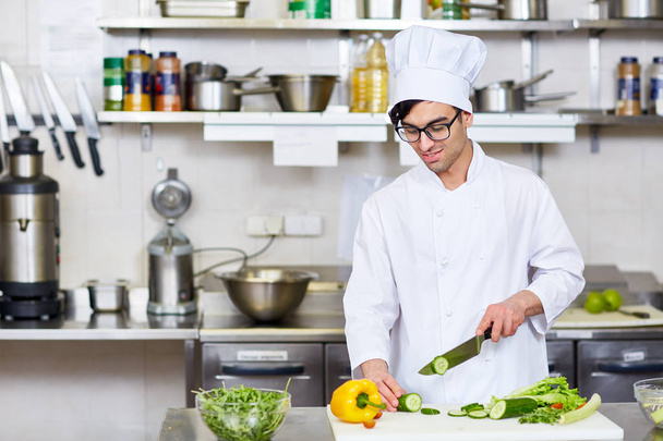 Chef en uniforme rebanando verduras frescas para ensalada
 - Foto, imagen