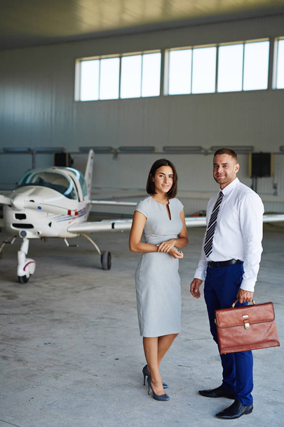 Portrait of smiling business people looking at camera while waiting in airport hangar, posing by jet plane - Foto, imagen