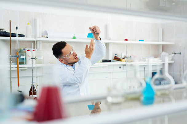 Portrait of modern scientist working in research laboratory, checking chemical reaction in test tube with colored liquid - Photo, Image
