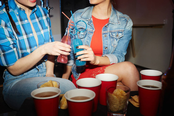 Портрет двух красивых девушек, звенящих коктейлями на вечеринке ночного клуба
 - Фото, изображение