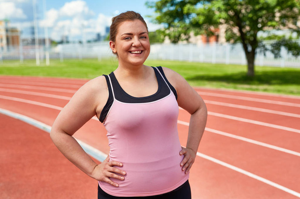 Happy young overweight female in activewear having training on stadium - Foto, Imagen