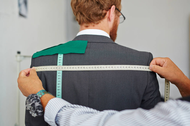 Old tailor taking back measurements from client in small atelier studio to make suit with jacket - Photo, Image