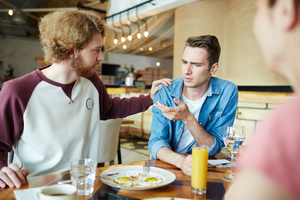 Νεαρός άνδρας καθησυχαστική ανησυχούν φίλο του κατά τη διάρκεια γεύματος στο καφέ - Φωτογραφία, εικόνα