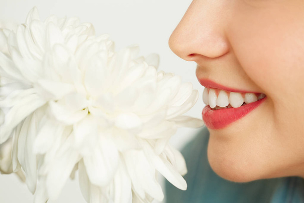 Profile view of smiling young woman with red lipstick enjoying smell of fresh chrysanthemum, close-up shot - Fotó, kép