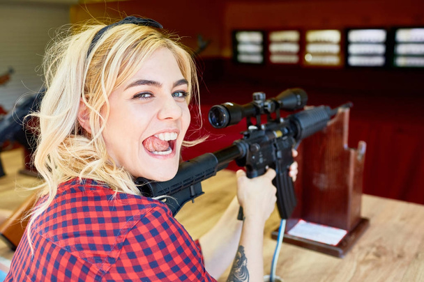 Portrait de fille blonde effrontée tenant un gros fusil au stand de tir dans un parc d'attractions
 - Photo, image