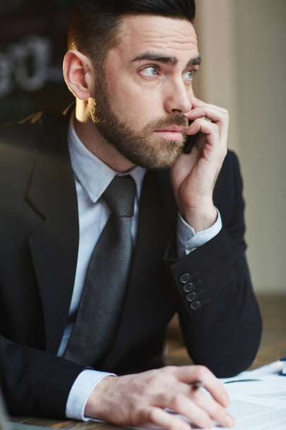 Retrato de homem de negócios barbudo moderno fazendo telefonema enquanto trabalhava no escritório na mesa
 - Foto, Imagem