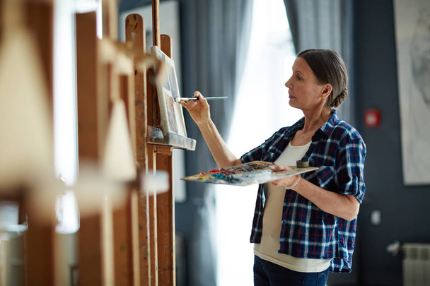 Portrait of elegant mature woman painting oil picture with inspiration in art studio - Foto, Imagem