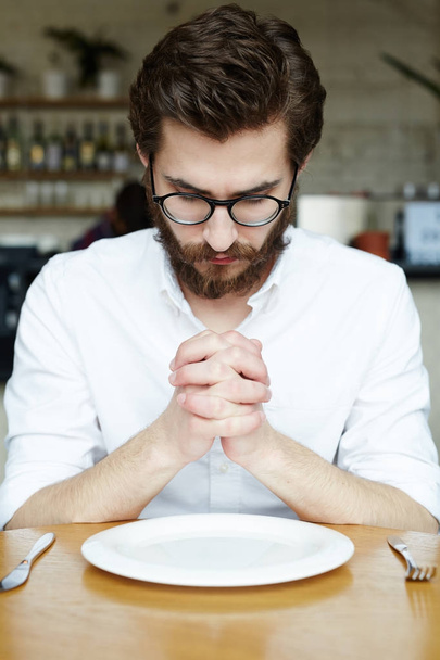 Jeune homme priant sur une assiette vide à la pause déjeuner
 - Photo, image