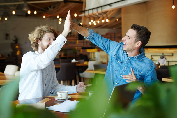 Two friendly guys giving high-five while spending time in cafe - Photo, Image