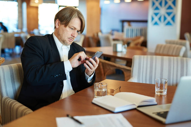 Porträt eines selbstbewussten Angestellten mittleren Alters, der während seiner Arbeit im Cyber-Café die Nummer seines Geschäftspartners wählt - Foto, Bild