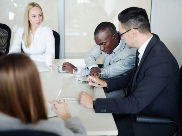 Grupo multiétnico de personas de negocios que se reúnen en la sala de conferencias: discutir temas corporativos y usar el teléfono inteligente en la mesa
 - Foto, Imagen