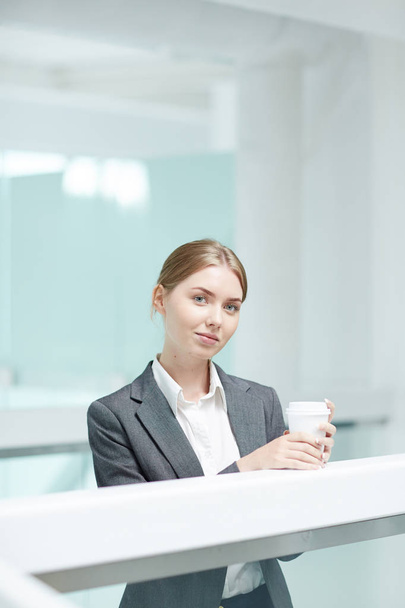 Waist-up portrait of attractive young manager in formalwear posing for photography while enjoying fragrant coffee at spacious office lobby - Foto, Imagen