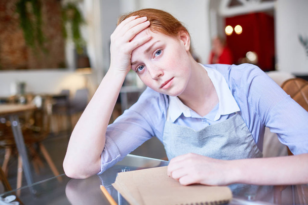 Zmęczona i smutna kelnerka siedzi przy stole po pracy - Zdjęcie, obraz