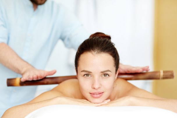 Kalm brunette geniet van massage opgebouwd met houten stok in dag spa salon - Foto, afbeelding