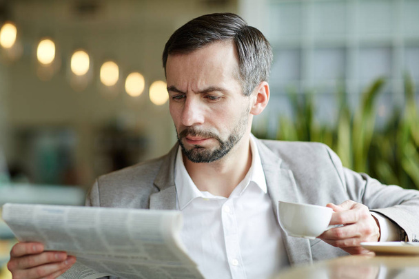 Serious and busy man with cup of tea reading morning news in cafe - Foto, Imagen
