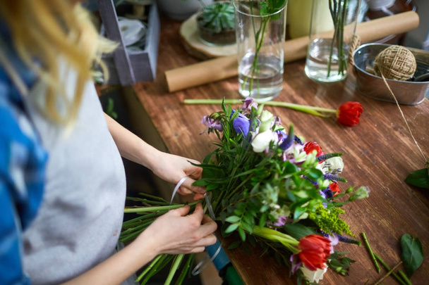 Female florist arranging bouquet and tying it with thin ribbon - Photo, Image