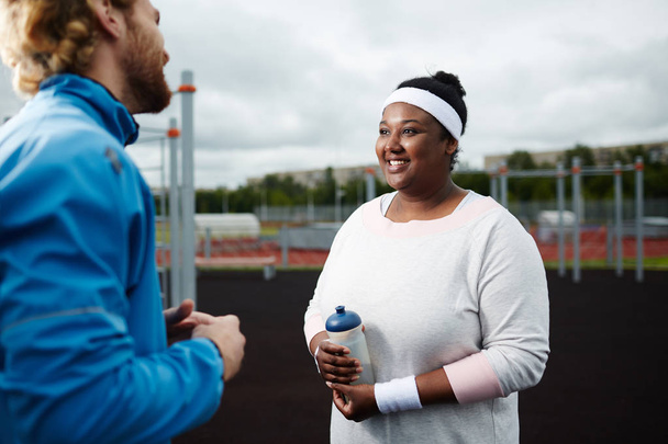 Felice giovane over-size donna parlando con il suo allenatore al campo sportivo
 - Foto, immagini