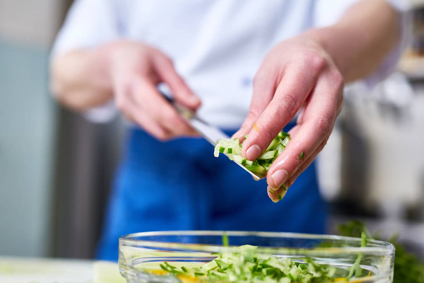 Vrouw zetten gesneden komkommers in de kom met salade - Foto, afbeelding