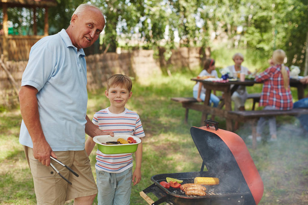 Boy and mature man making bbq during family hangout - 写真・画像