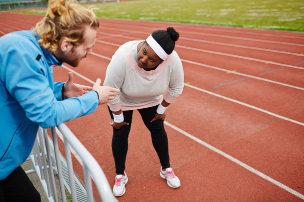 Молодая спортивная девушка плюс размер слушает советы тренера во время тренировки на стадионе
 - Фото, изображение