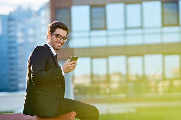 Young broker texting in smartphone outdoors - Fotó, kép