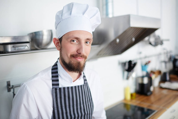 Propietario de panadería en uniforme de chef mirando a la cámara en la cocina
 - Foto, Imagen