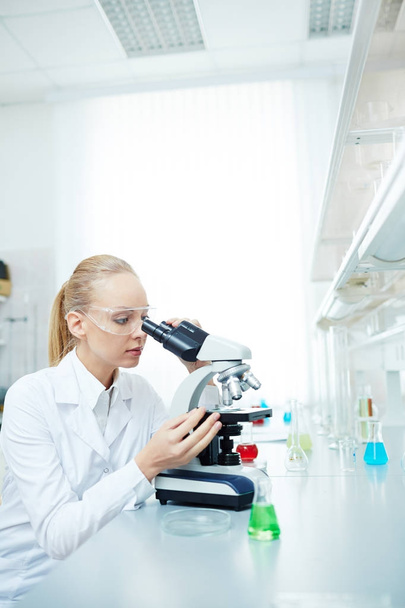 Retrato de una hermosa científica usando microscopio trabajando en investigación médica en laboratorio moderno
 - Foto, imagen