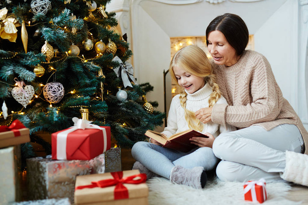 Cute girl reading book of xmas tales with her grandmother at home - Foto, Imagem