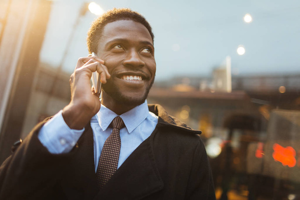 Hymyilevä mies puhuu älypuhelimeen ulkona
 - Valokuva, kuva