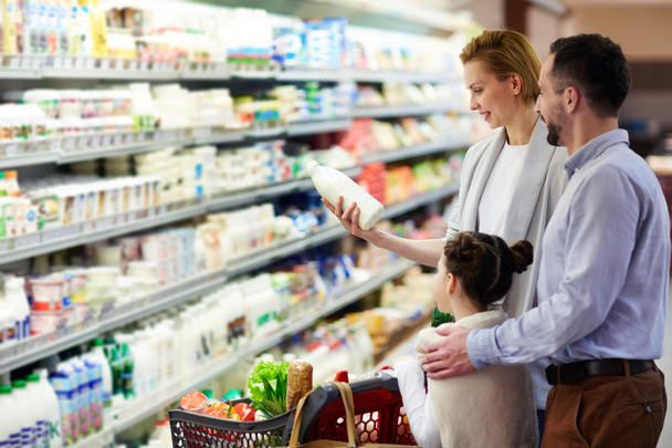 Portrait of happy family shopping in grocery store: buying milk in dairy product department - Фото, изображение