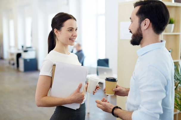 Portret uśmiechający się młoda kobieta rozmawiać z kolegą podczas przerwy w biurze, zarówno holding kubki kawy papieru - Zdjęcie, obraz