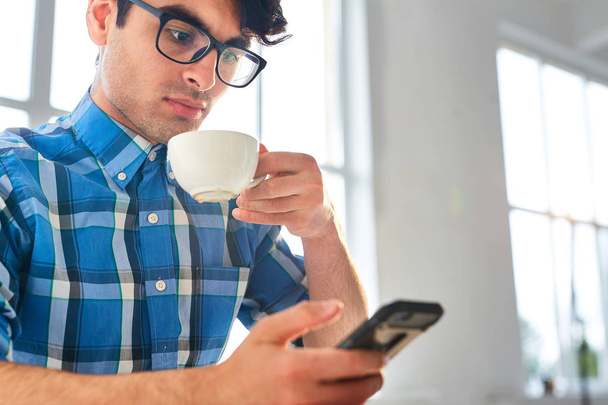 Młody człowiek z telefon komórkowy wiadomości i o filiżankę kawy - Zdjęcie, obraz